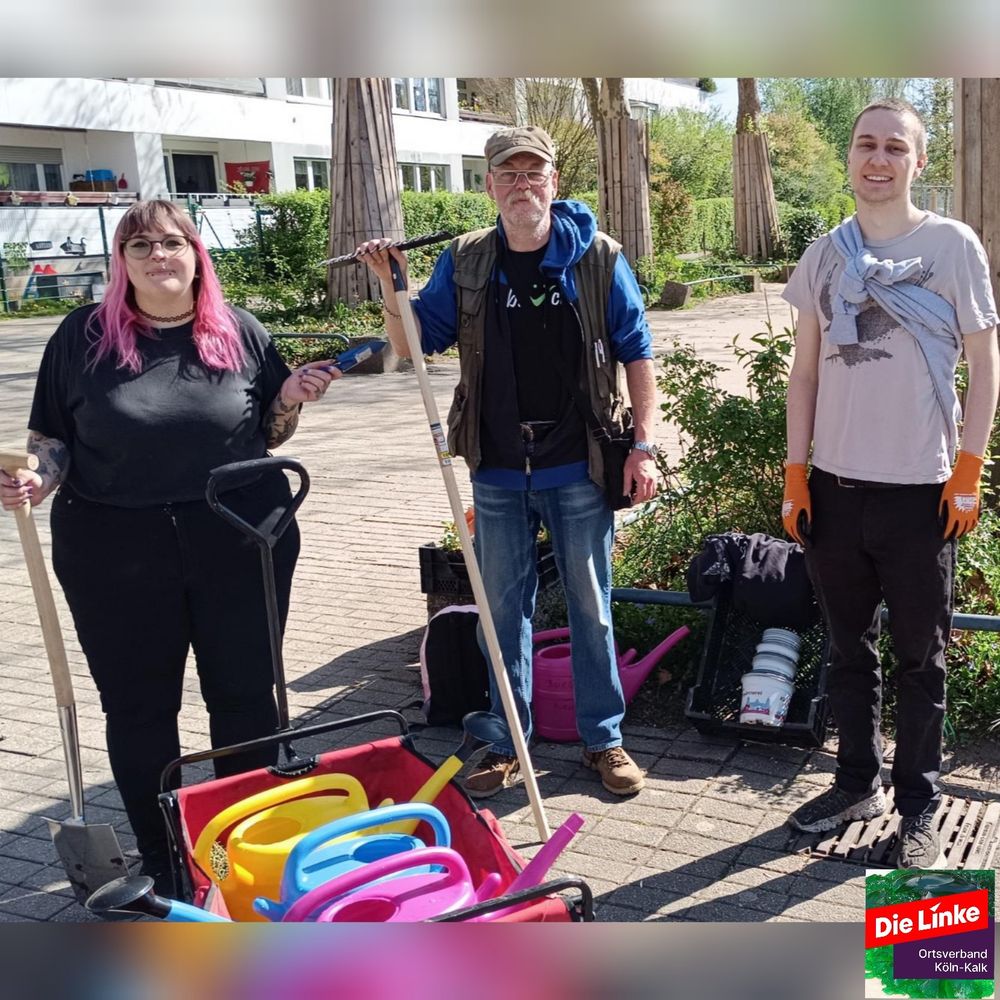 Das Bild zeigt drei Personen, die sich an einem sonnigen Tag auf einem Platz vor einem Wohnhaus befinden und offensichtlich Gartenarbeiten durchführen.  Zwei Personen halten Gartengeräte wie Spaten und Rechen. Gießkannen befinden sich in einem roten Bollerwagen. Im Hintergrund ist ein Wohnblock sichtbar.  Ein Logo der Partei „Die Linke“ im Ortsverband Köln-Kalk ist im unteren rechten Bildbereich zu sehen.