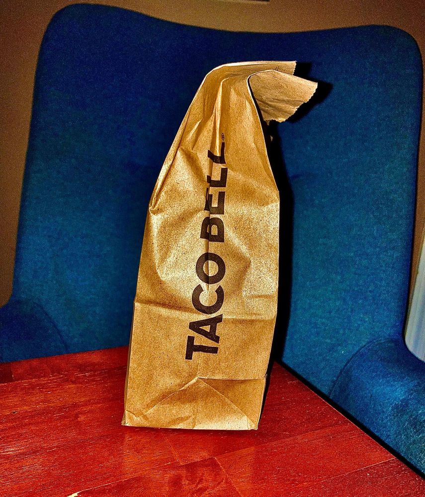 taco bell bag on a wooden table in front of a chair. this photo is edited, natch. feel free to reuse & adapt. cc by sa 