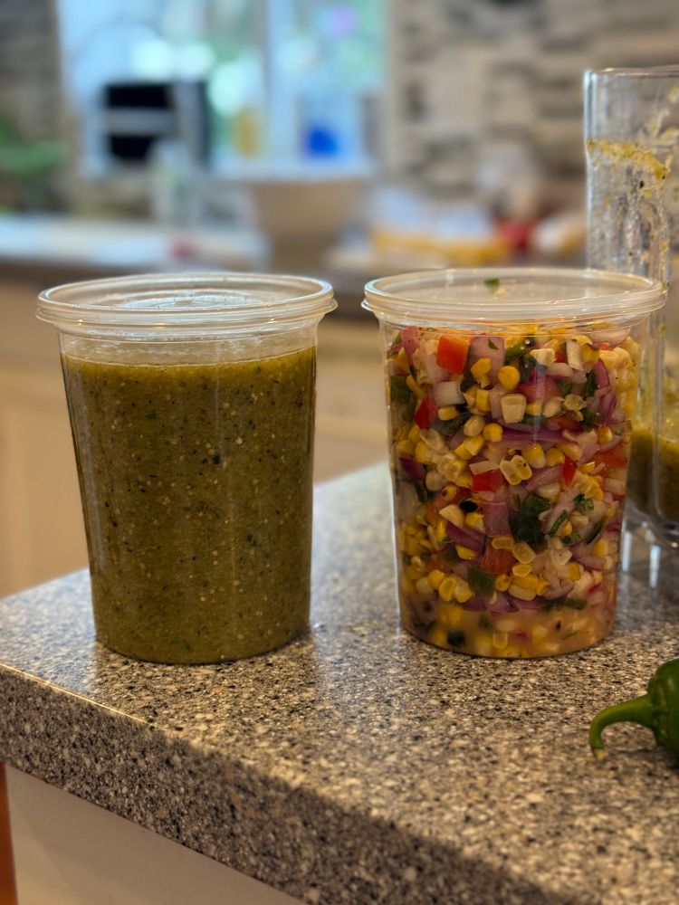 Two quart containers, one of salsa verde, one with roasted corn and poblano salsa. 