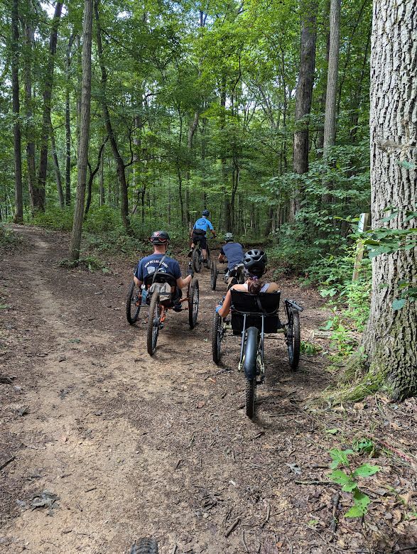 Three mountain bikers on adaptive bikes and a ride leader on a regular bike in Schaeffer Farm, MD