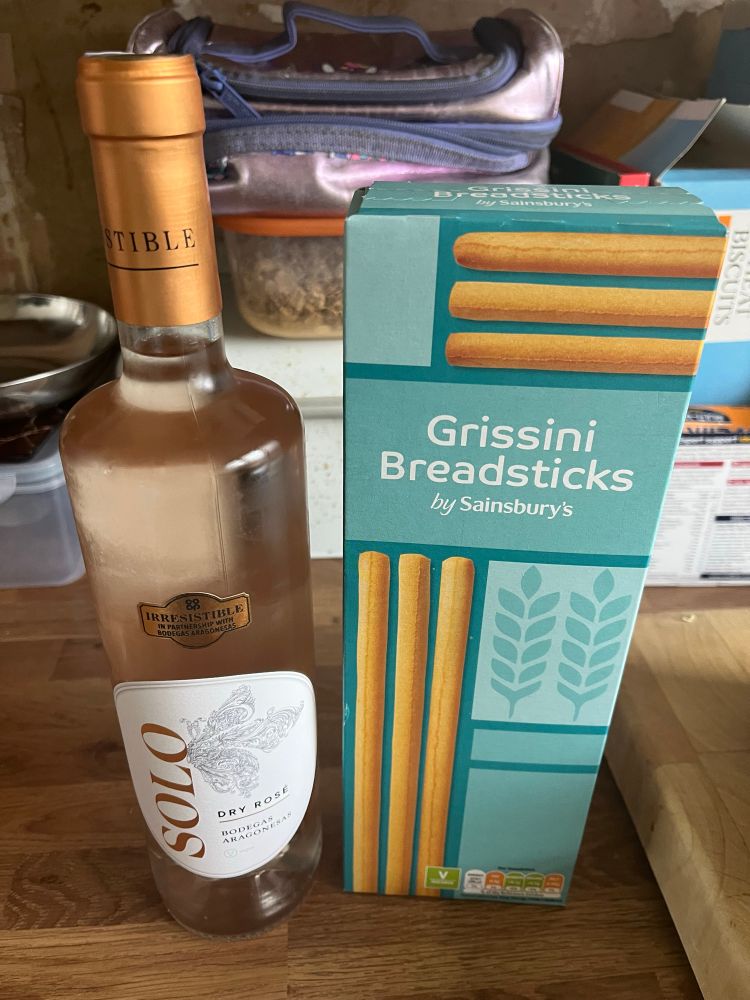 Tall bottle of rose wine alongside a box of Sainsbury’s plain breadsticks.