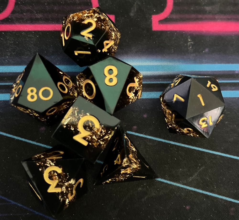 Set of DnD dice, black with gold sparkles and gold numbers. The D20 is showing a natural one.