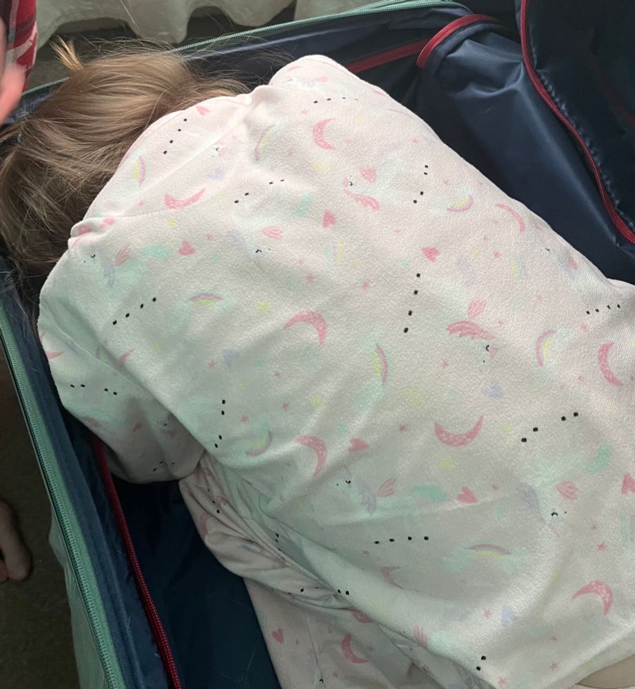 A small girl in pink pyjamas curled up with her head down and back to the camera in our suitcase.