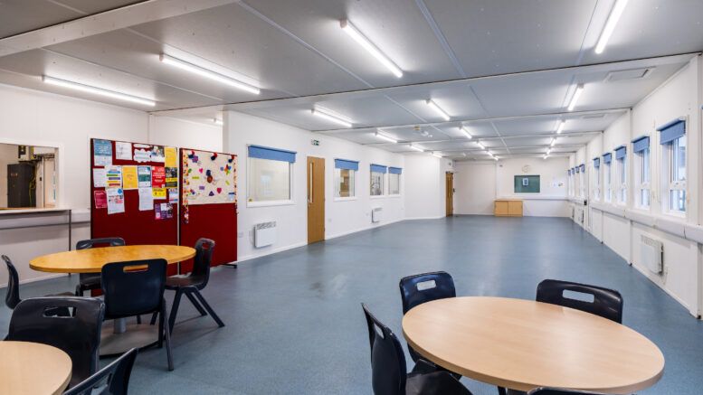 Inside the Alf Marshall Centre. A large indoor space with a handful of circular tables and chairs. Posterboards line the far wall with posters on.