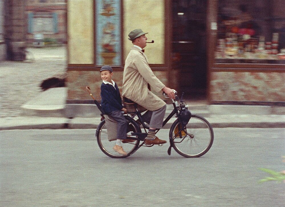 Jacques Tati, in character as Monsieur Hulot, wears an overcoat, pants that are too short, and ridiculous socks as he pedals his bicycle through the Parisian Quartier, an old neighborhood that the filmmaker contrasts with the mechanized, modern world. A cute little boy, Hulot’s nephew, rides on the back of the bike, absorbing the unfamiliar naturalness of the old neighborhood.