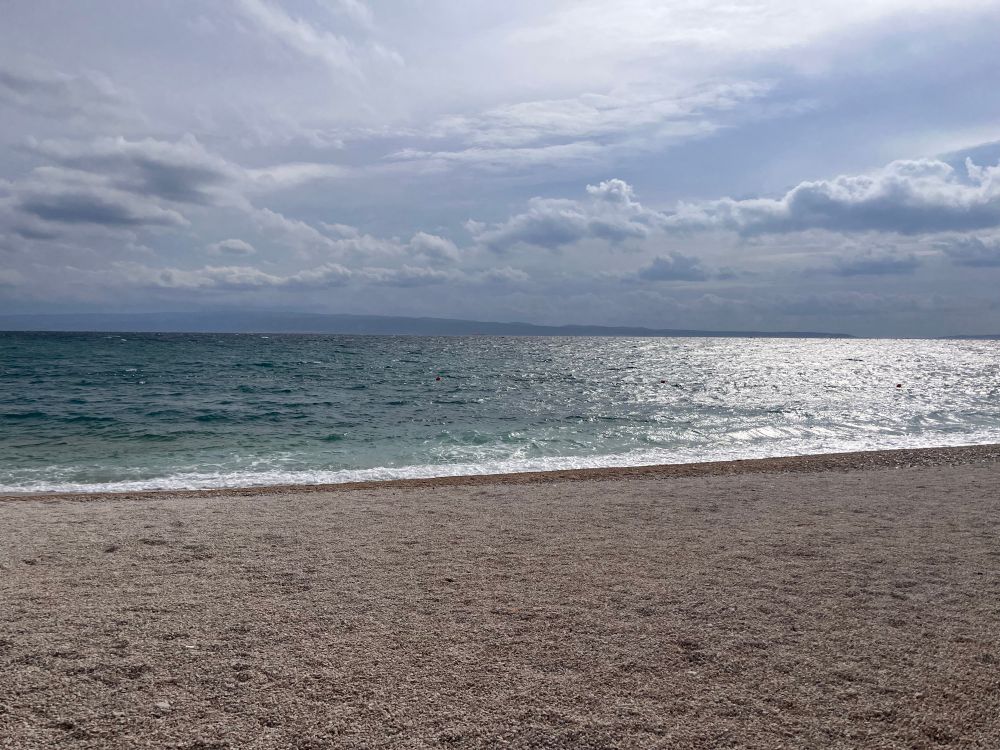 Foto vom Strand. Man sieht türkises meer an einem Kiesstrand.  