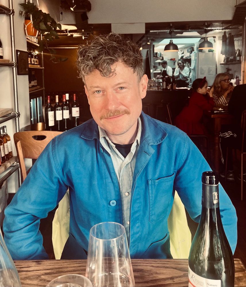 Photo of me, curly hair and a moustache, wearing a blu du trevail in the People’s Wine wine bar on Roman Road