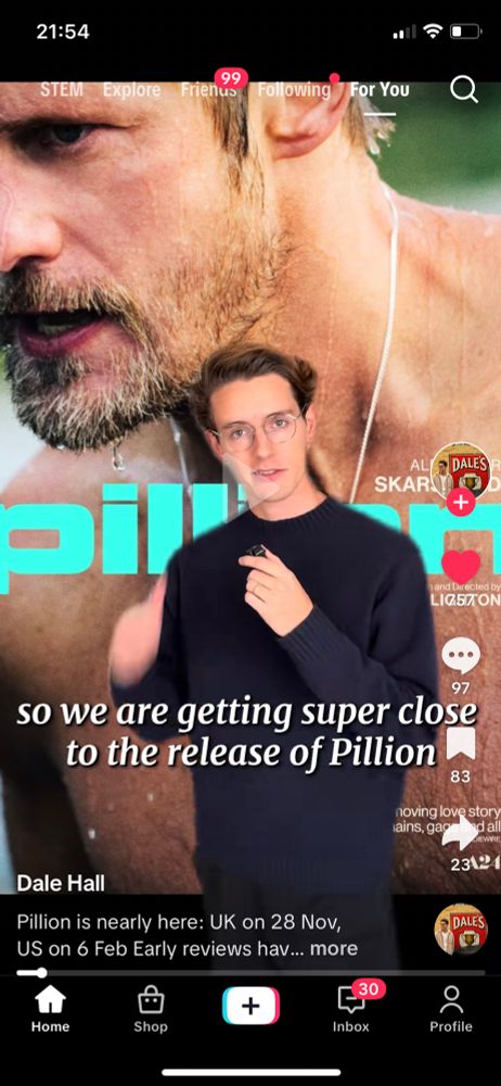 Screenshot of TikTok. Somebody in the foreground is talking about a new film called Pillion. On the poster for the film being them, is a handsome slightly beardy masc person with their top off. 
