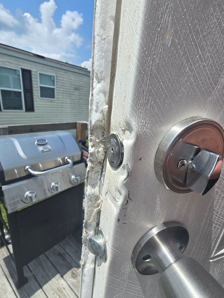 Photo of a white door that is warped and marked where a pry bar has apparently been wedged around the locks