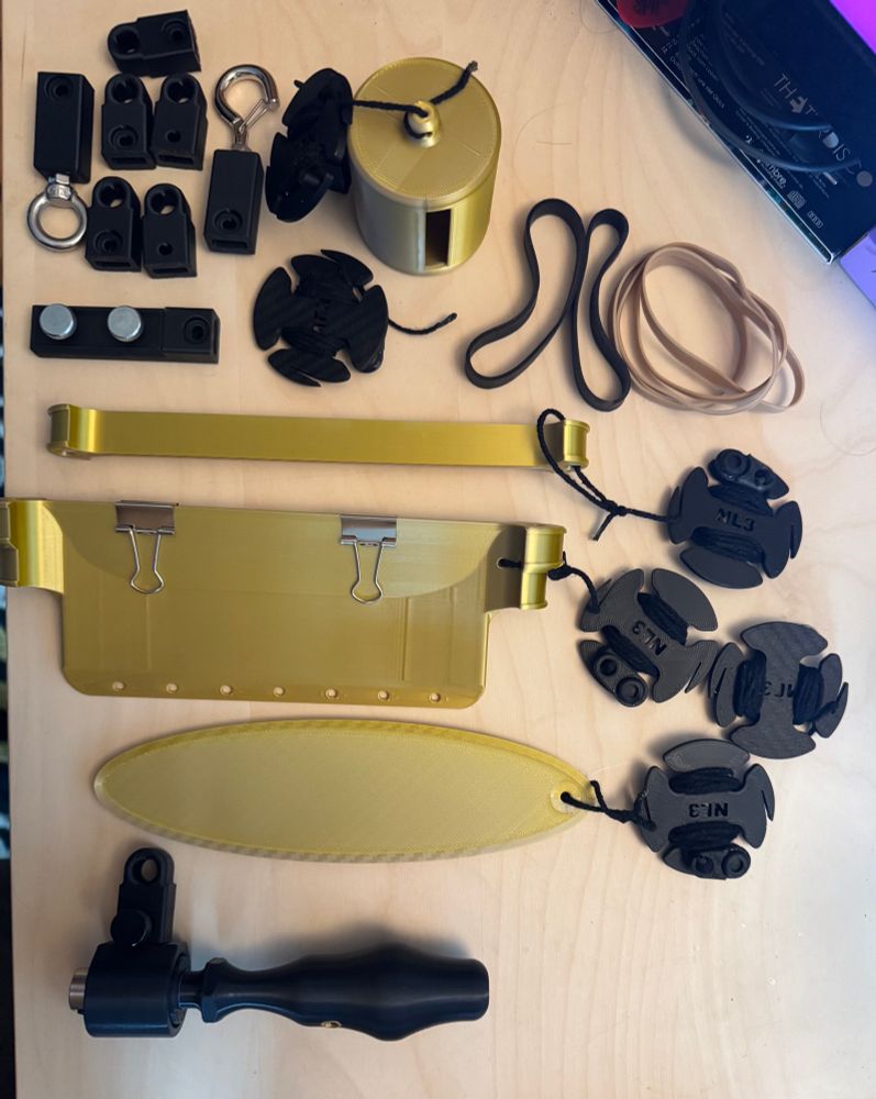 The Foley flinger and its components laid out on a table, various hooks, bullroarers, and other contraptions that attach to the device and can be whirled around thanks to a solid ball bearing mounted on a sturdy handle.