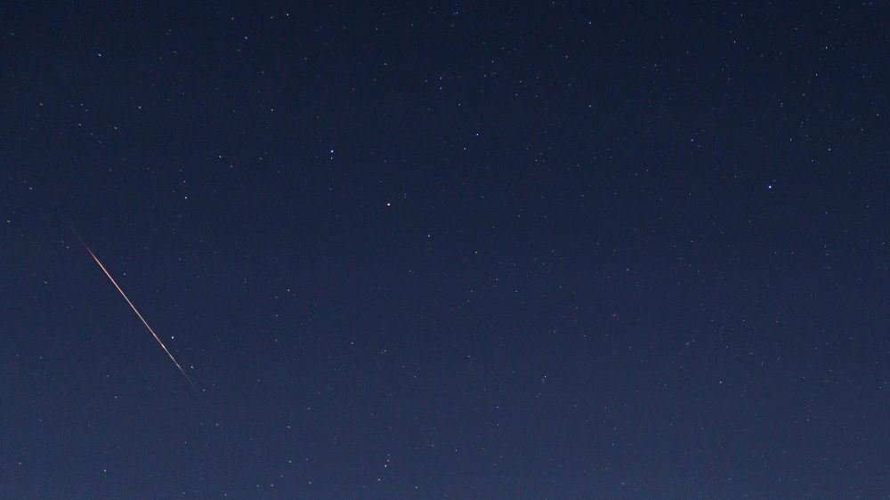 A bright orange meteor passing close to the stars of Ursa Minor. The Pole Star, Polaris can be seen to the right of the image, with the meteor to the left. The sky is a deep blue colour due to the bright moonlight on the night of 9-10 August 2025 when the shot was taken. Settings: 10s exp, 18mm fl, f/3.5, ISO-800. Time: 23:35 UT on 9 August.