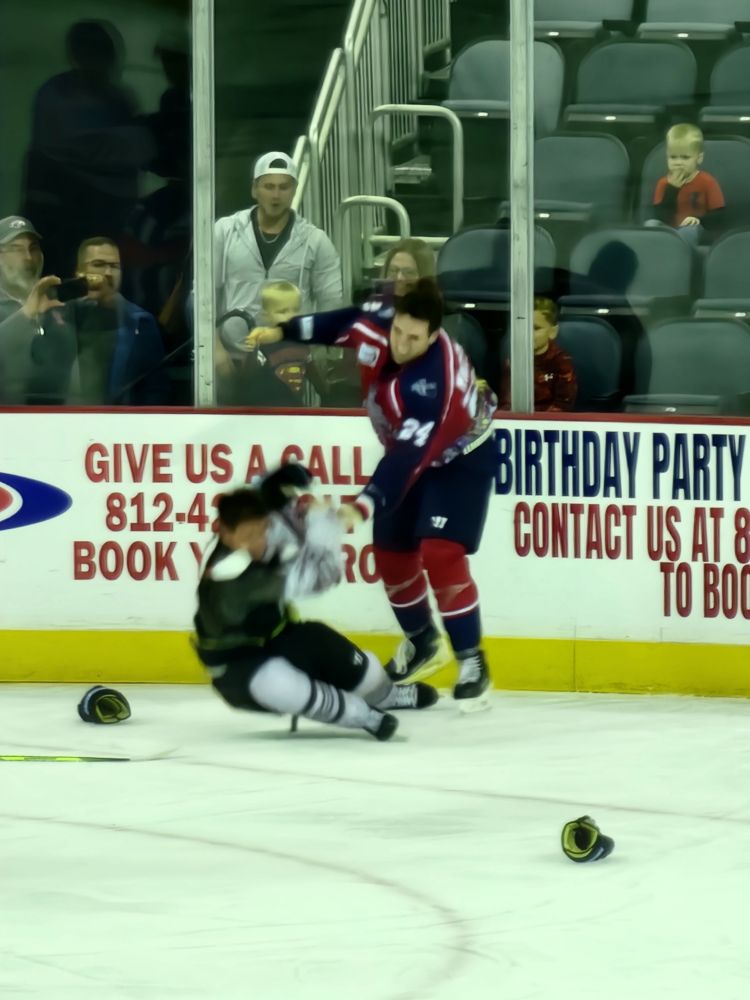 Quad City hockey player falling to the ice after a fight with an Evansville Thunderbolts player in the corner behind the Bolts' net