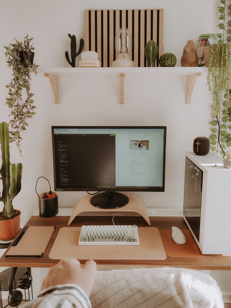 Photo of desk station straight ahead. Green plants and  minimalist decor on a shelf above the desk. White PC on desk, green keyboard caps.