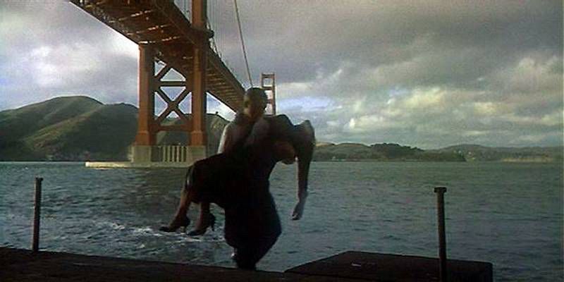 A still from Vertigo; a man carrying an unconscious woman in his arms away from the water under the Golden Gate Bridge 