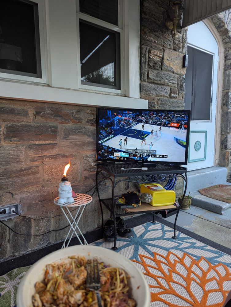 A TV set up on a porch with a bowl of boy slop in the foreground 