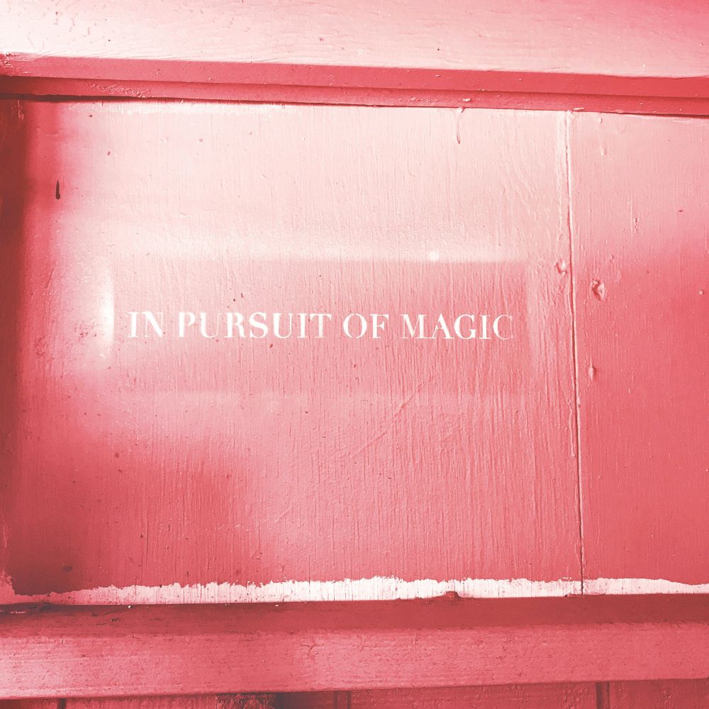 Some kind of wood painted pink. On it it says in stenciled white letters: In Pursuit Of Magic.
