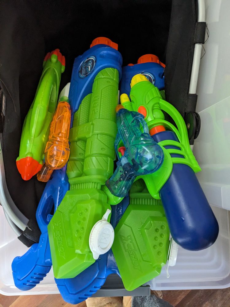 A black basket with an assortment of 6 lurid green, blue and orange coloured water pistols.
