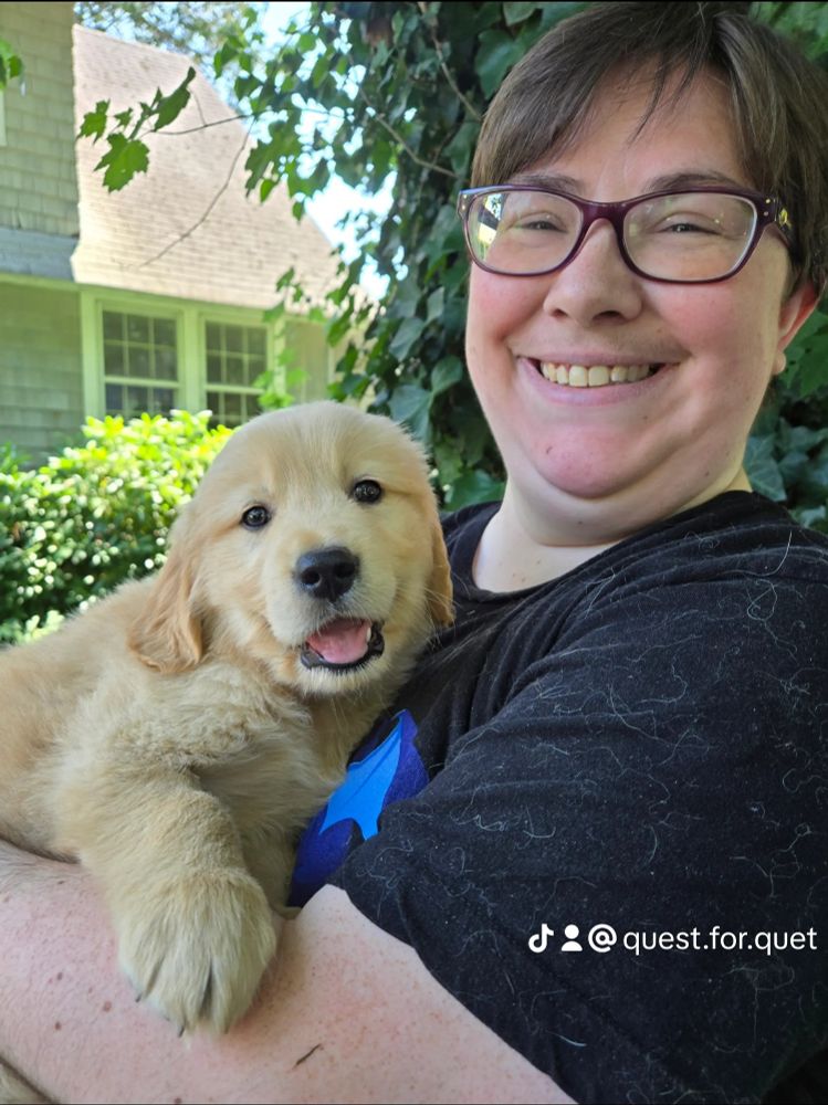 A photo of a white human in a black t-shirt is holding a 5 week old golden retriever puppy. Both are smiling at the camera. There's a TikTok logo in the bottom right with the tag @ quest.for.quet