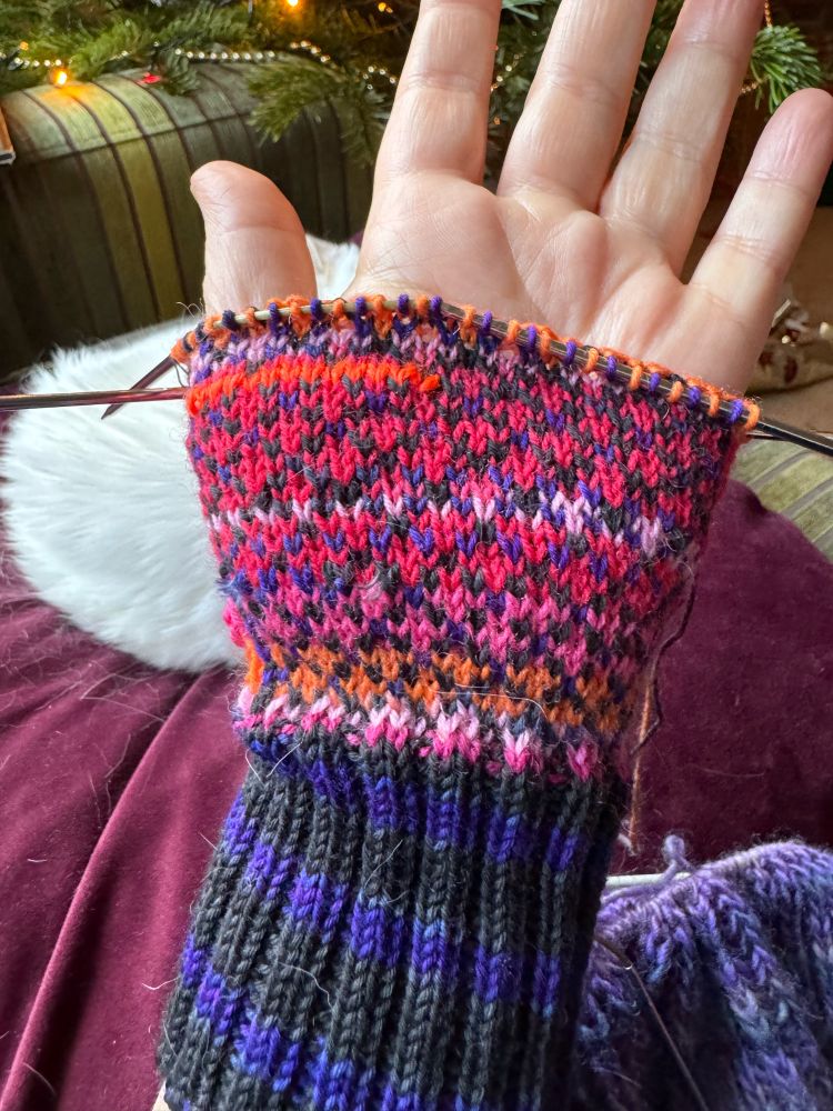 Half finished mitten in Nordic pattern, using black/purple and shades of pink yarns, palm  side