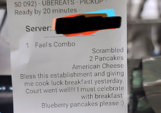 An UberEats order ticket with a customer comment stating “Bless this establishment and giving me good luck breakfast yesterday. Court went well!!! I must celebrate with breakfast. Blueberry Pancakes please :-)”
