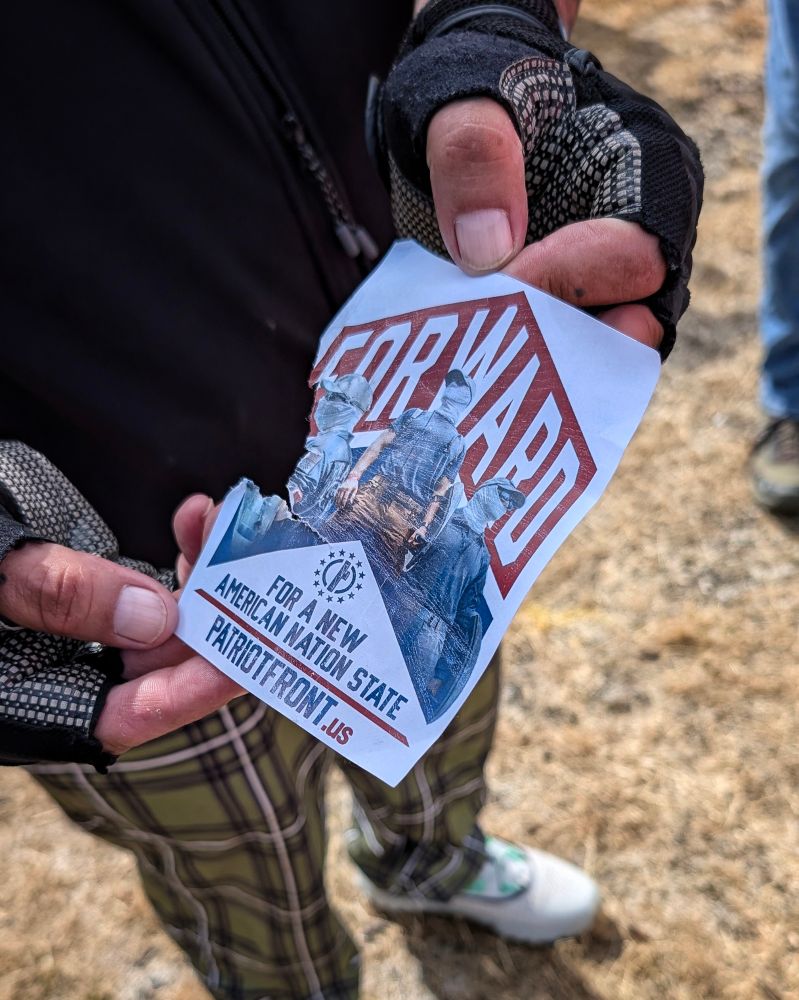 A person's hands holding a torn sticker with a Patriot Front design on it.