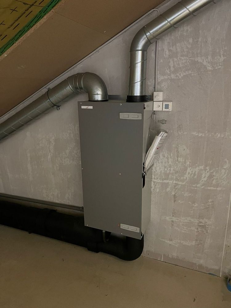 Zehnder ComfoAir 200 Lüftungsgerät mit Wärmetauscher, welches an einer Wand angebracht und mit 4 Wickelfalzrohren an Zu-/Abluft innen/aussen (Rohre mit Isolation umhüllt) angeschlossen ist.