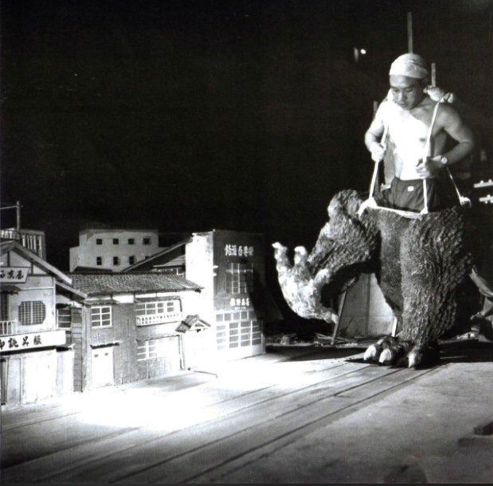 Haruo Nakajima, the actor inside the rubber suit of Godzilla, stomping down the street of a miniature set of Tokyo wearing the lower half of the Godzilla suit