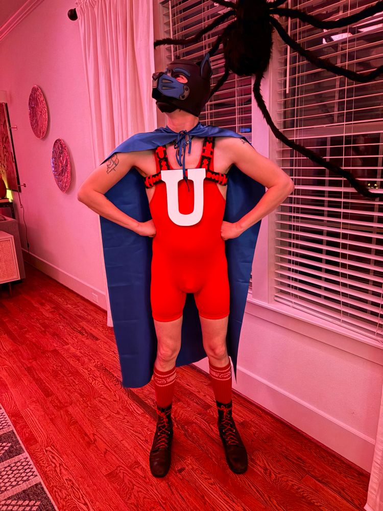 Human pup wearing a red singlet, a blue cape, and a big white U on the chest like the character Underdog.. 