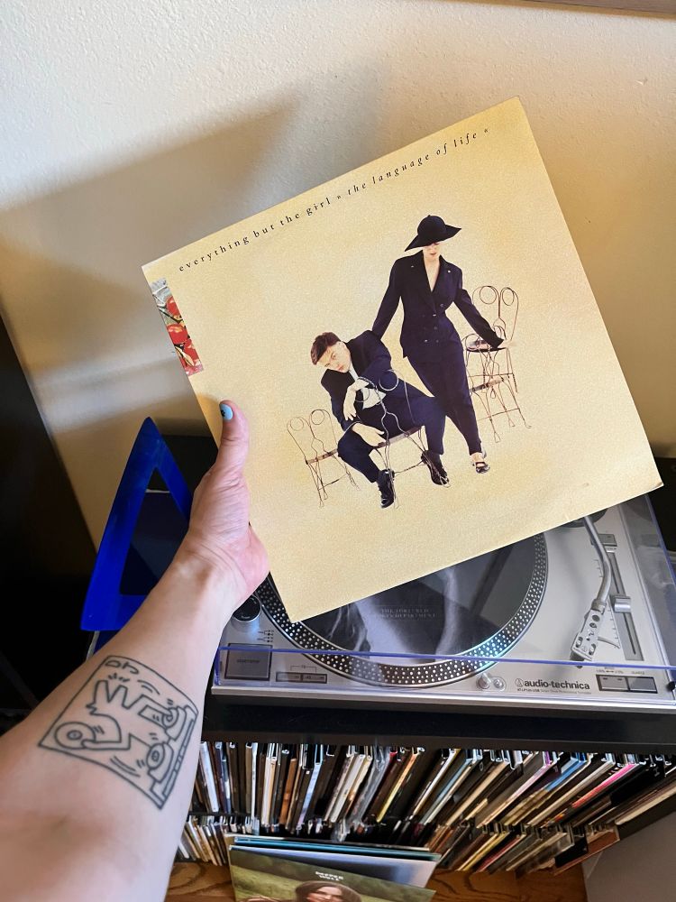 An extended arm holds a copy of The Language of Life by Everything But The Girl over a record player. 
