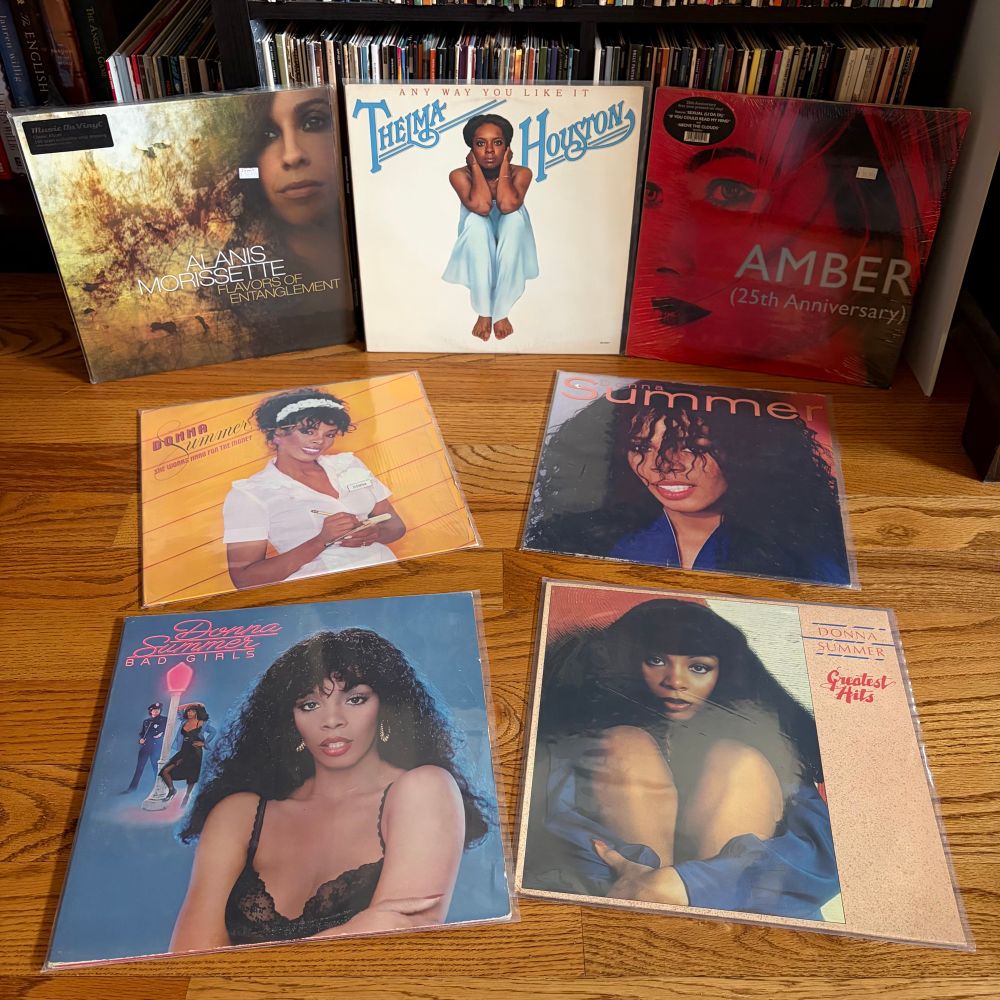 7 vinyl albums are laid out. Flavors of Entanglement by Alanis Morrisette, Amber (25th Anniversary), Any Way You Like It by Thelma Houston. And by Donna Summef: Bad Girls, She Works Hard for the Money, self-titled, and Greatest Hits