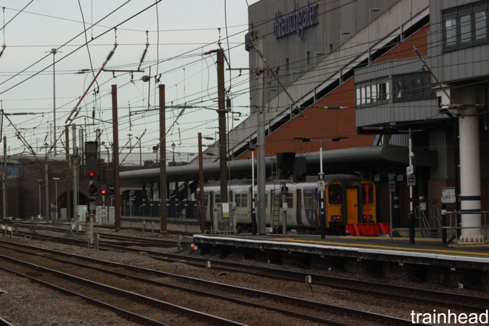 Northern Class 150 at Doncaster, with a big building in the back and a bunch of overhead wires