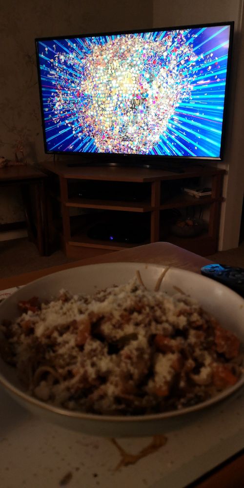 A bowl of spaghetti Bolognese sprinkled with parmesan in the foreground with Strictly Come Dancing on the TV in the background.