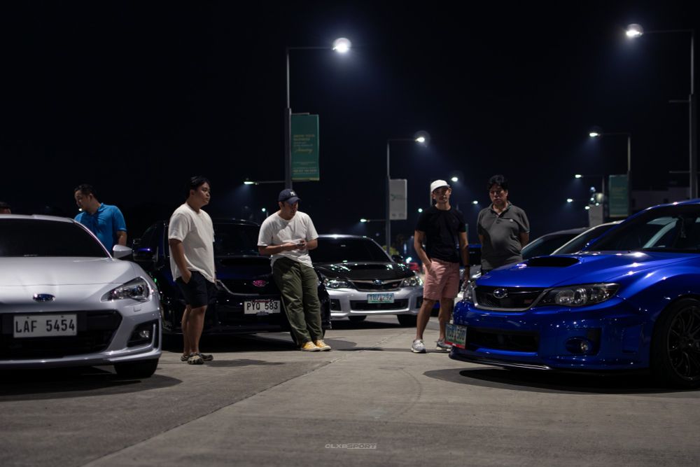 people hanging around a car meet with Subaru Imprezas and a BRZ parked around them.