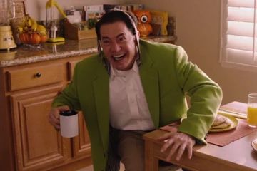 dougie jones holding a cup of coffee with a tie on his hand and he’s in complete disarray as a crazed smile spreads across his face 