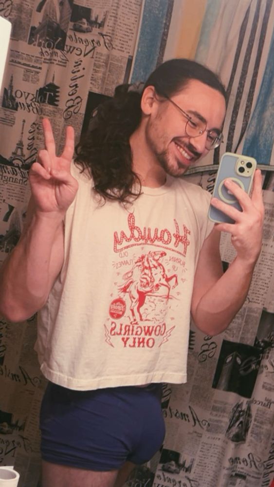 in a mirror with purple underwear and a cropped tank top that has a cowboy and horse rearing back that says “howdy, cowgirls only” when she gave it to me she said “i know you’re cowboys too but the shirt was cute”