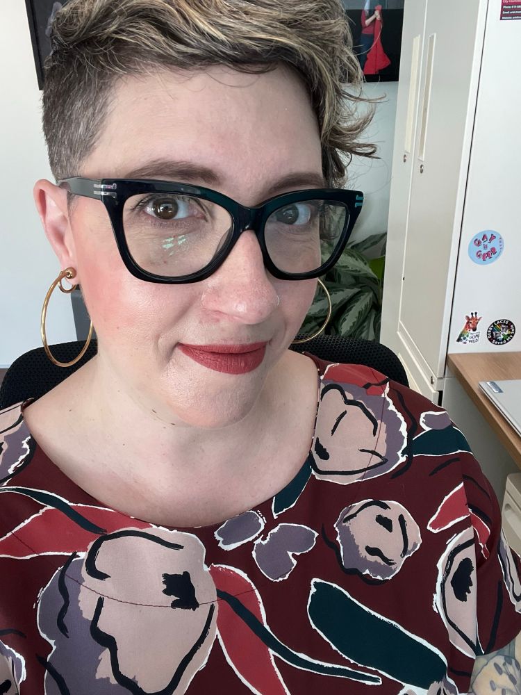 Ariel, wearing a floral dress, black cat eye glasses and hoop earrings 