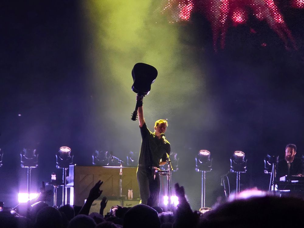 Ben Gibbard on stage holding an acoustic guitar above his head