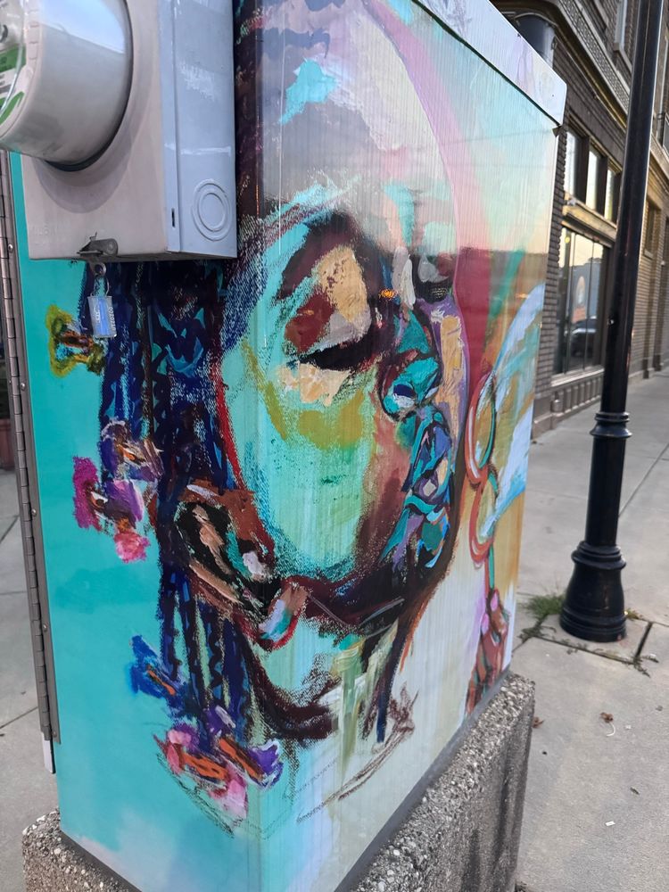 Dayton Ohio. 5th and Keowee. Street art on an electrical box of a Neighborhood child with braided hair, each braid ends with a different colored bow.