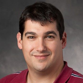 Professional headshot of an individual in a maroon shirt, smiling slightly at the camera.