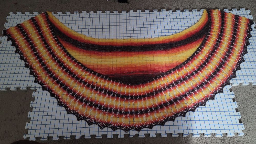 A newly-knitted shawl with bold colors, spread out over foam blocks and pinned in place to dry