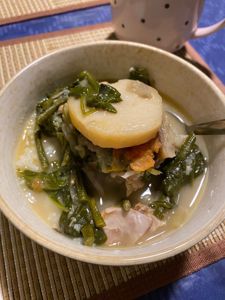 Bowl of sinigang with gabi (white taro) on top. Visible contents of dish include spinach, long beans, and pork.