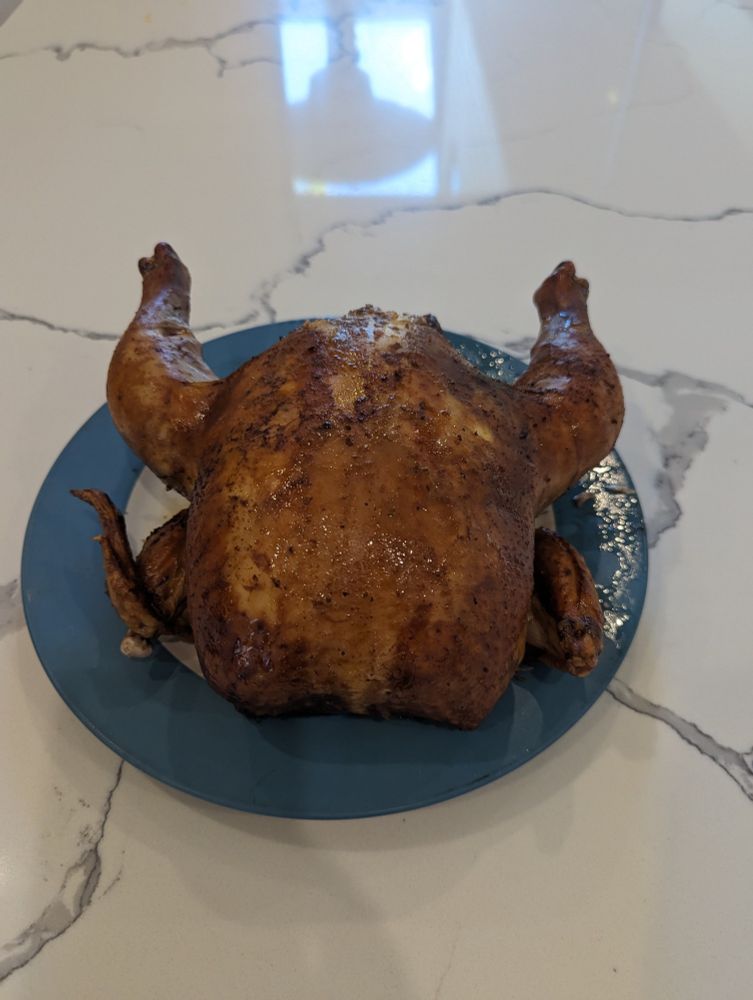 Beautiful smoked whole chicken on a blue plate on granite