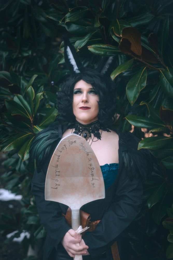 Me cosplaying my dnd character, Cassandra. I am holding a shovel that says "On raven's wings, one day you will fly." in Elvish. 