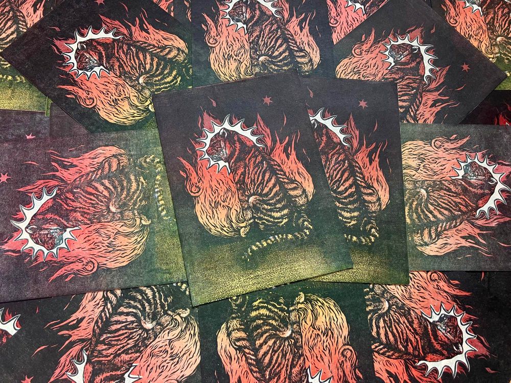 group of prints with tiger sitting in front of fire, colours are in gradient from magenta, through orange to yellow. tiger is looking to the left, there is a white star-like shape behind its head.
