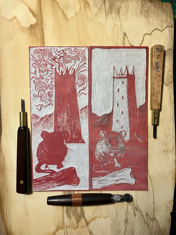 two carved linocut blocks with a mouse eating a bone and mountains, tall tower and clouds in the background. around the blocks are arranged two carving tools and a relief roulette