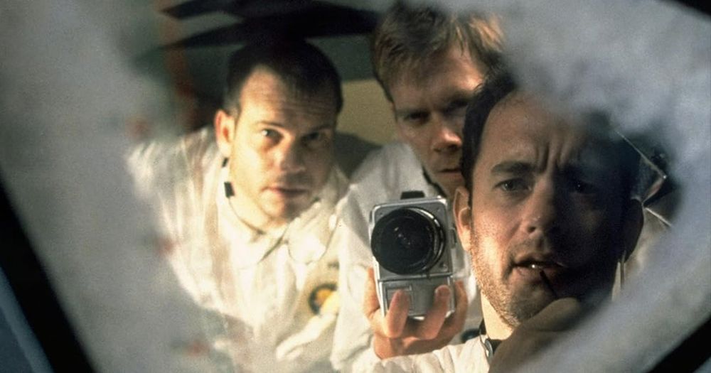 Tom Hanks, Kevin Bacon, and Bill Paxton, in astronaut suits, intently examining a cracked spacecraft window from the film Apollo 13.