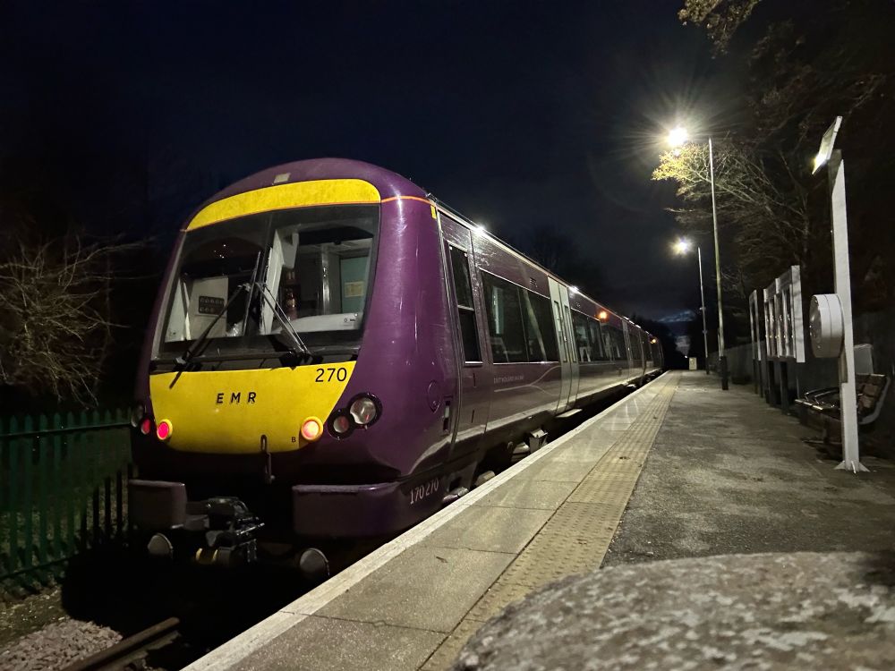 170270 in EMR purple livery stands in the platform at Barton in the dark - the platform is empty and stations lights are lit. The tail lights are lit on the unit.