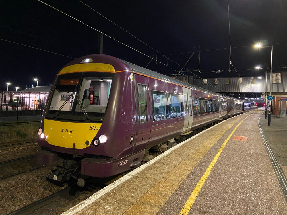 170504 in EMR purple livery under the ramp footbridge on platform 2 at Peterborough. It is dark and the platform is empty and you can see the red signals at the far ends of p1 and p2