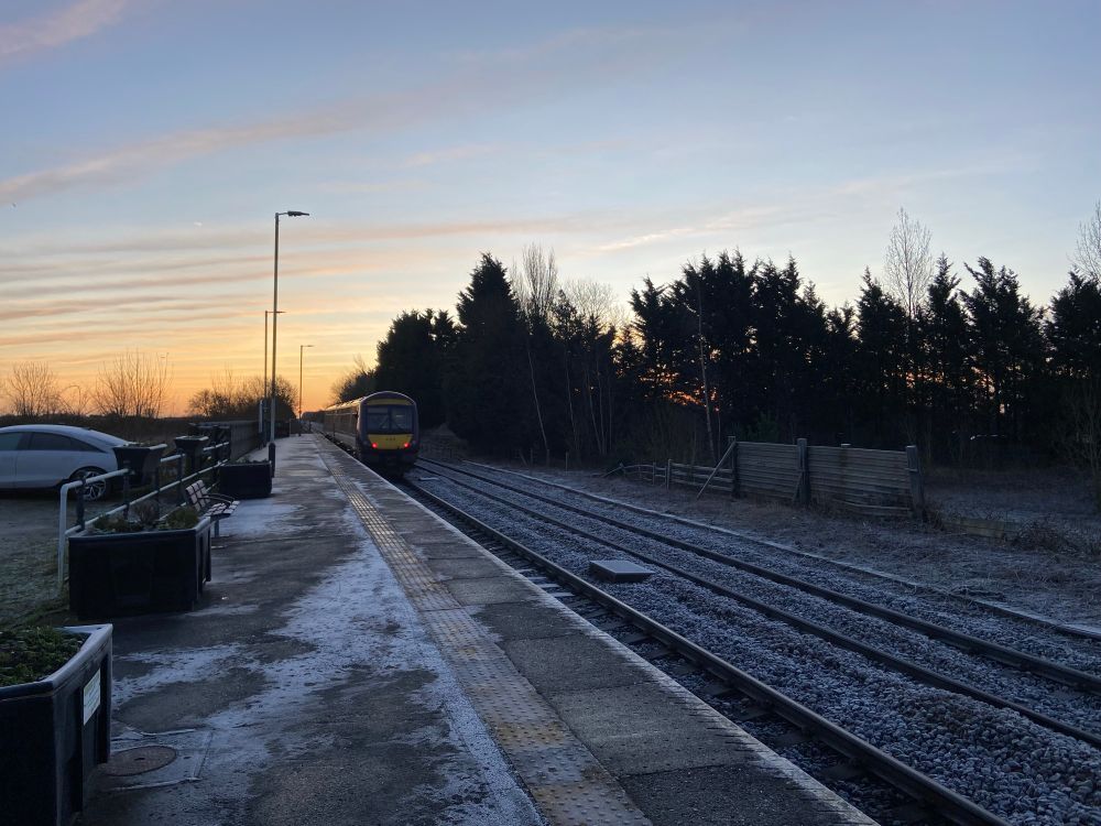 An EMR class 170 in purple departs into the red and blue sunrise from habrough station. A covering of frost sits on the platform and tracks.