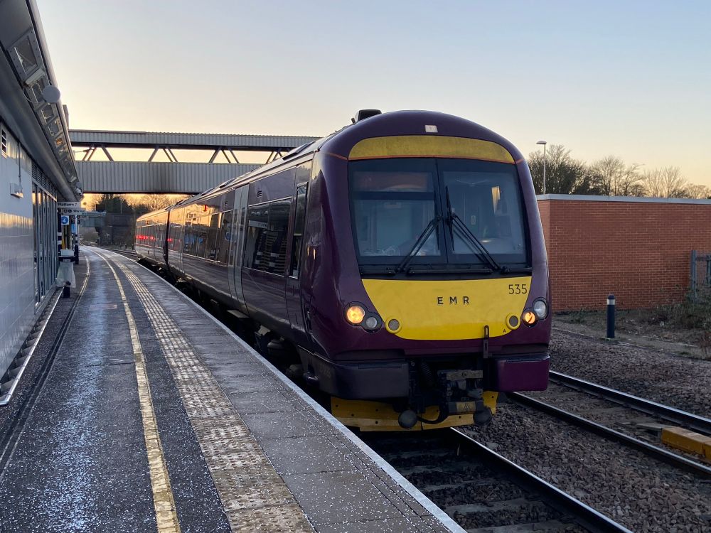 My purple EMR 170 535 in platform 7 at Peterborough station. The platform is empty of people and you can see the salt scattered along it. A red signal is reflected in the train windows. The sky is blue grey with the sun rising.